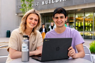 Two students sitting at a laptop outside a campus building